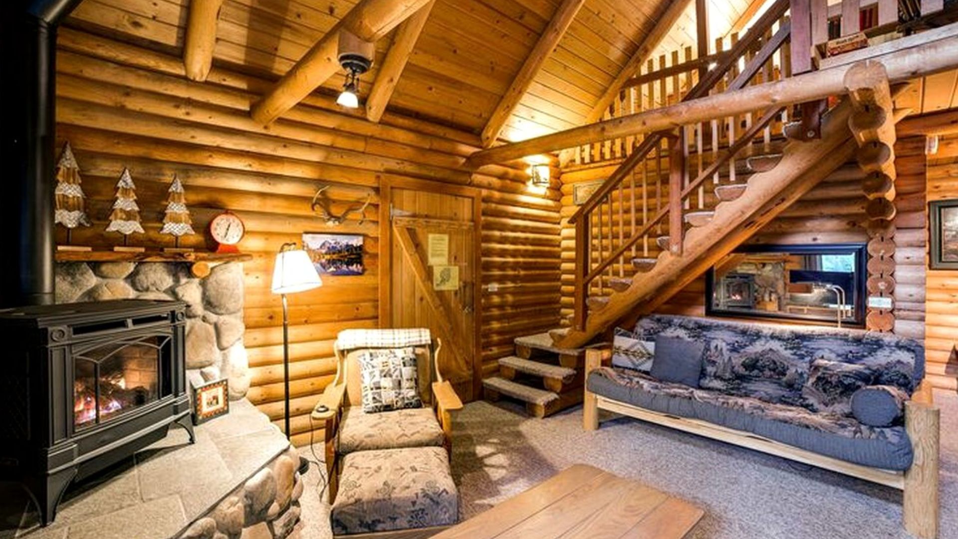 living room area with an armchair, a futon, next to a fireplace, and wooden stairs that lead upstairs in the back