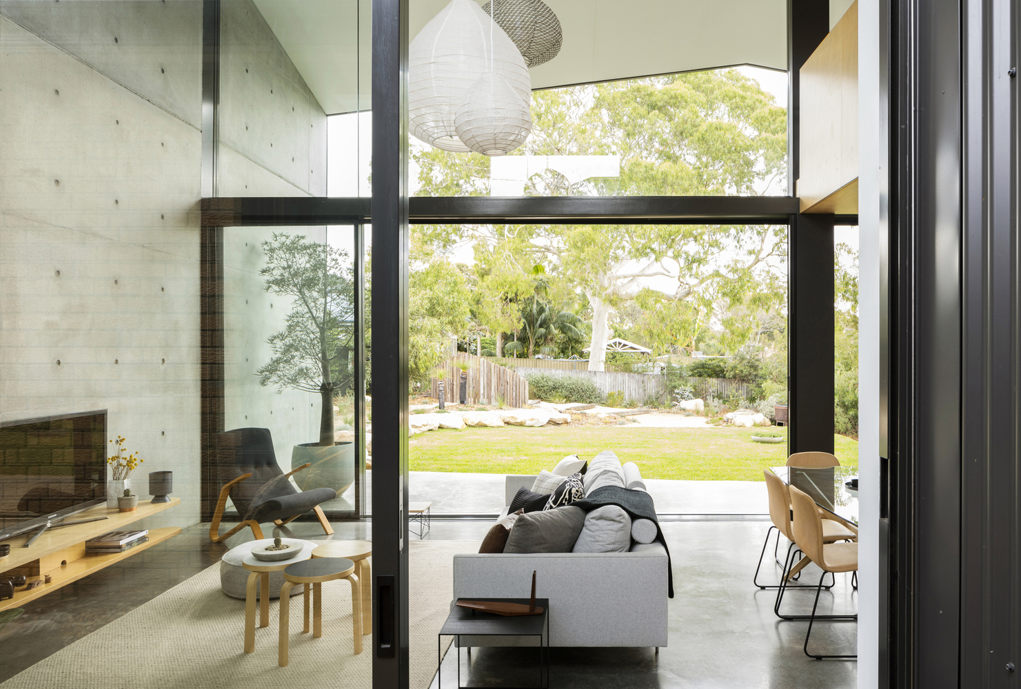 living room with a floor to ceiling window, flat screen tv, white couch and a chair in the corner of the room