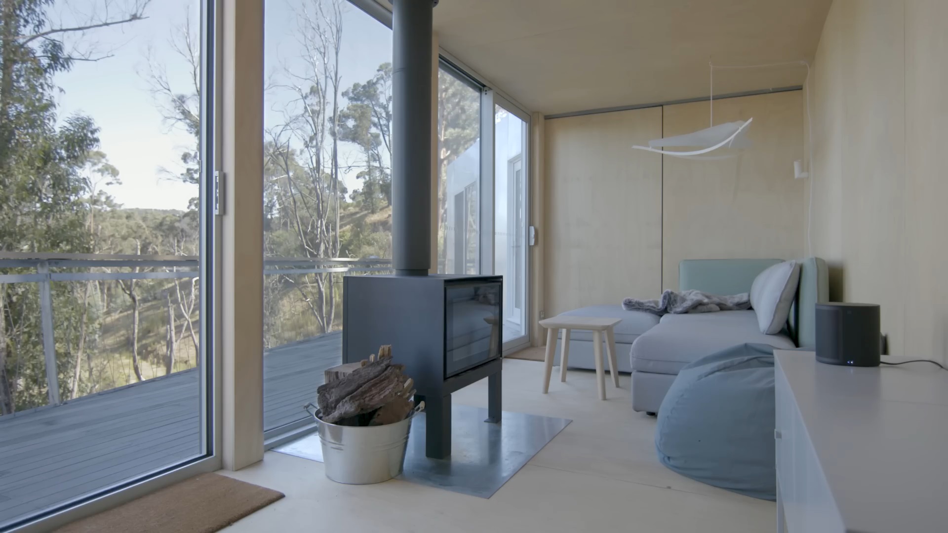 living room with a blue couch and a blue bean bag with floor to ceiling windows and a black fireplace and a small brown table