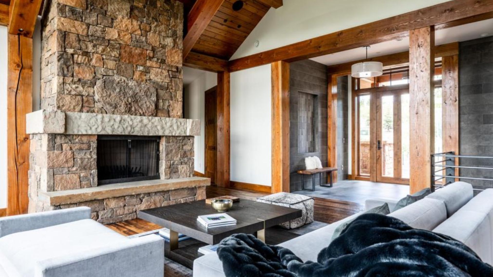 big living room with wooden beams, grey sofa, and a huge fireplace carved in stone