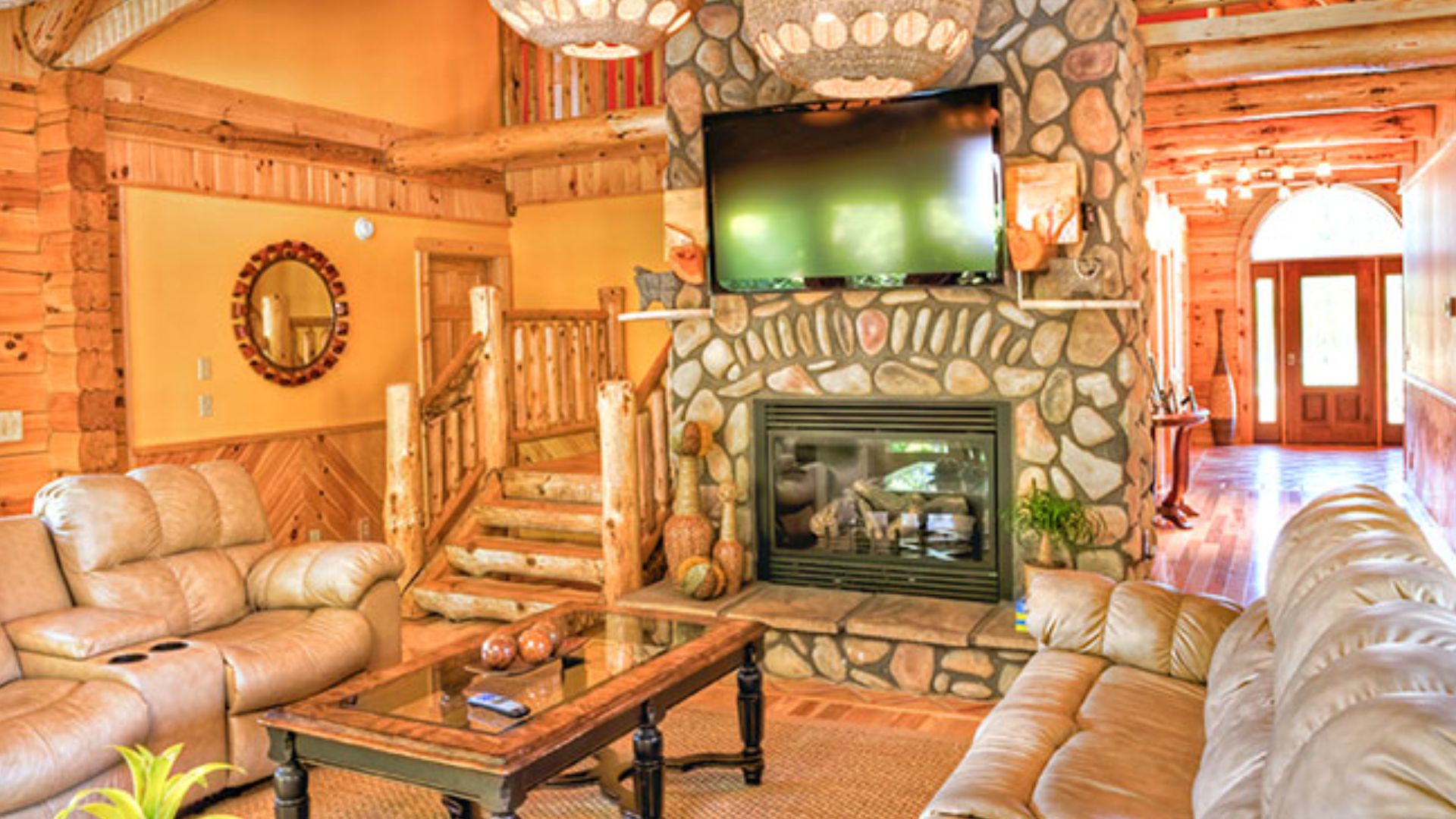 living room with cozy couches, log walls, exposed wood beams, and a massive stone fireplace