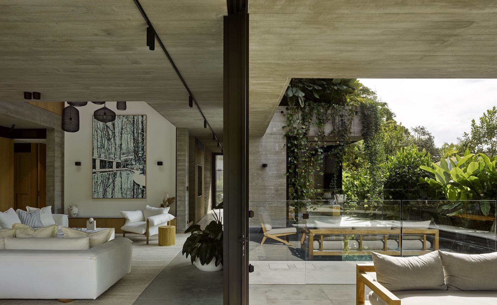 living room with a white couch and a chair, a big blue and white art piece on the wall, on the right is the outside area of the house with a pool