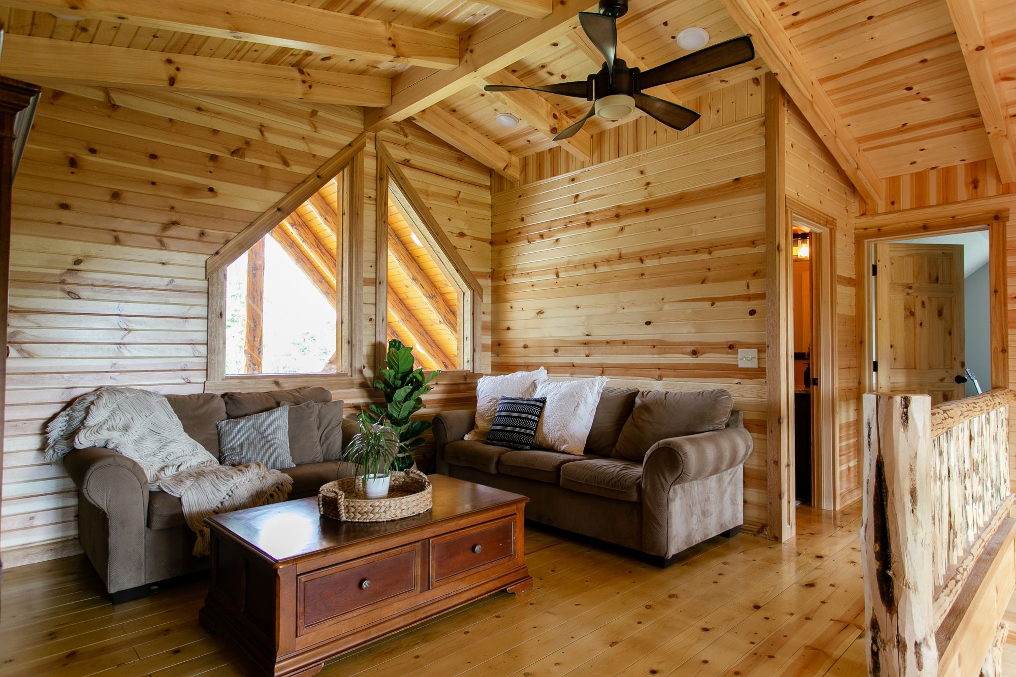 living room in a loft area, with two couches and a brown cabinet table and a ventilator on the ceiling