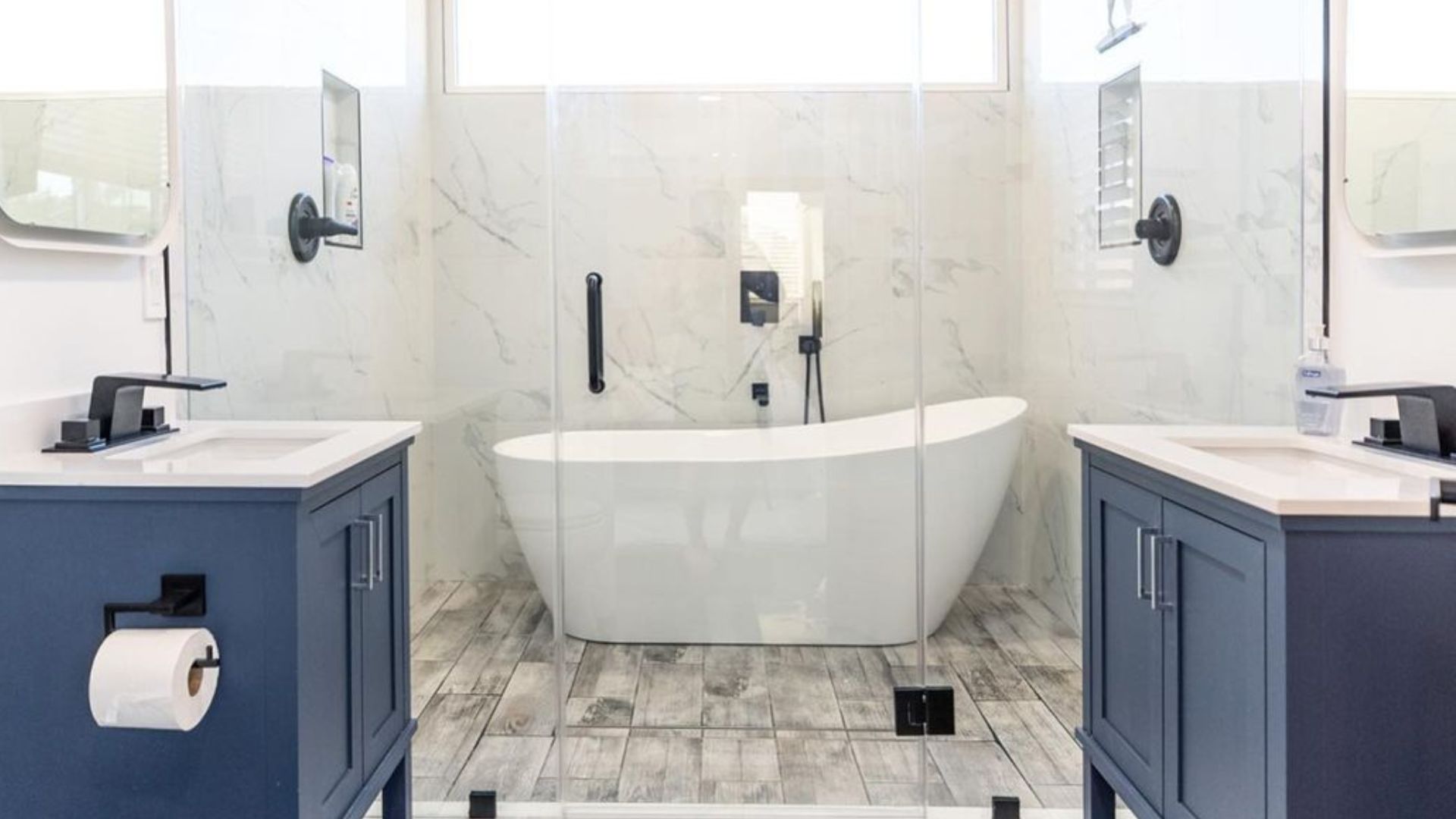 white bathroom with marble tiles, his and her blue vanities, and a stylish tub