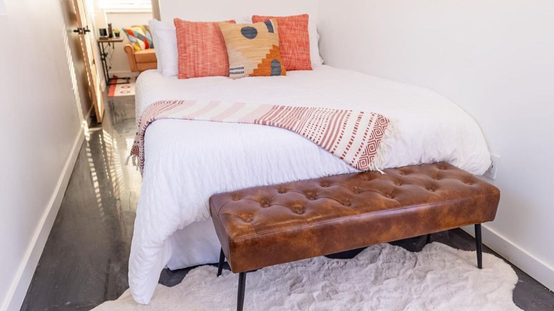 master bedroom with orange throw pillows, a leather bench, and a fuzzy rug