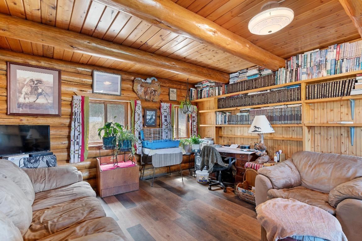 living room with gray couches, floor to ceiling shelf and an office area with a desk and a chair, and many photos on the wooden walls