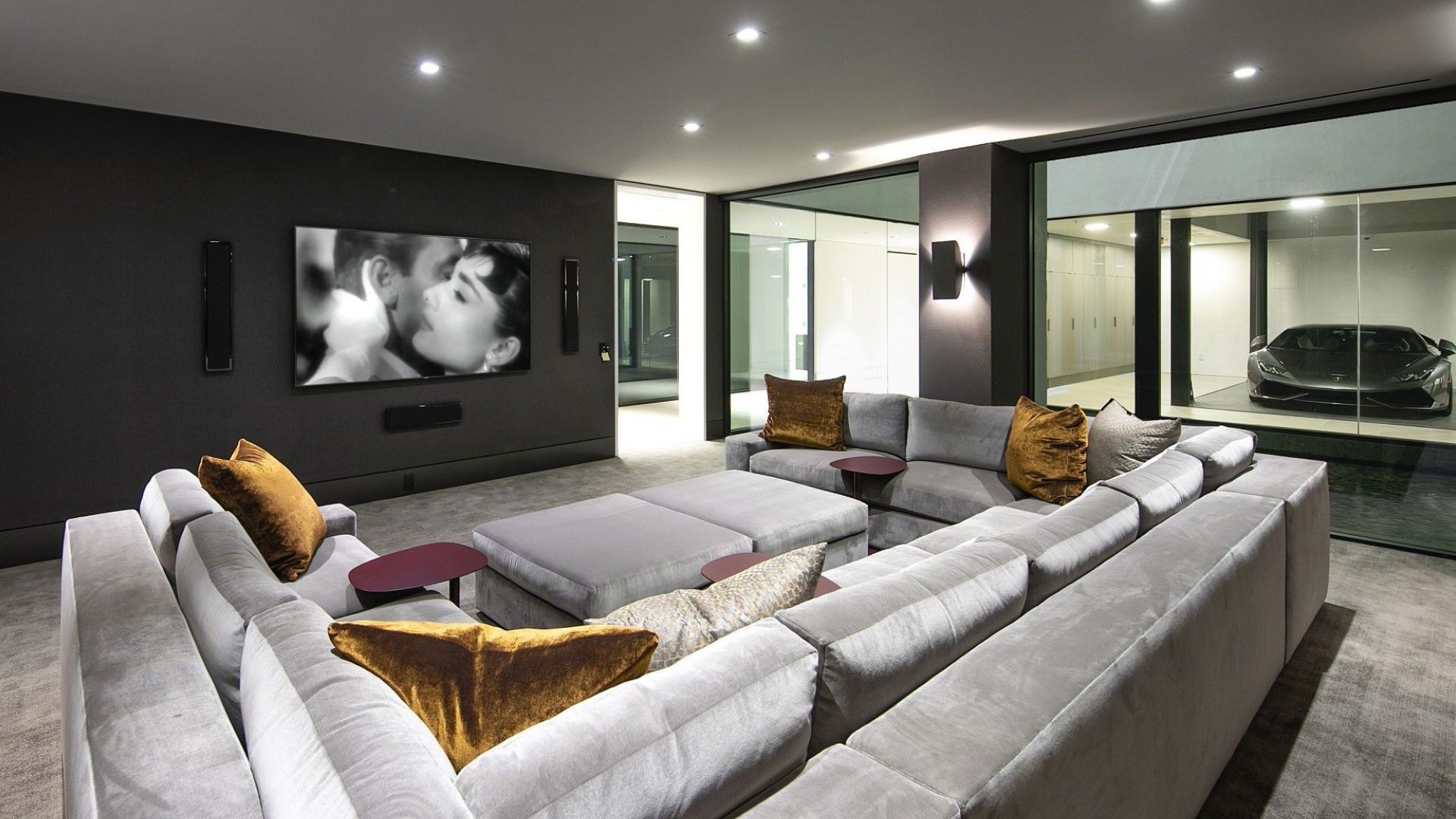 media room with a big grey sofa in the basement right next to a garage with glass walls