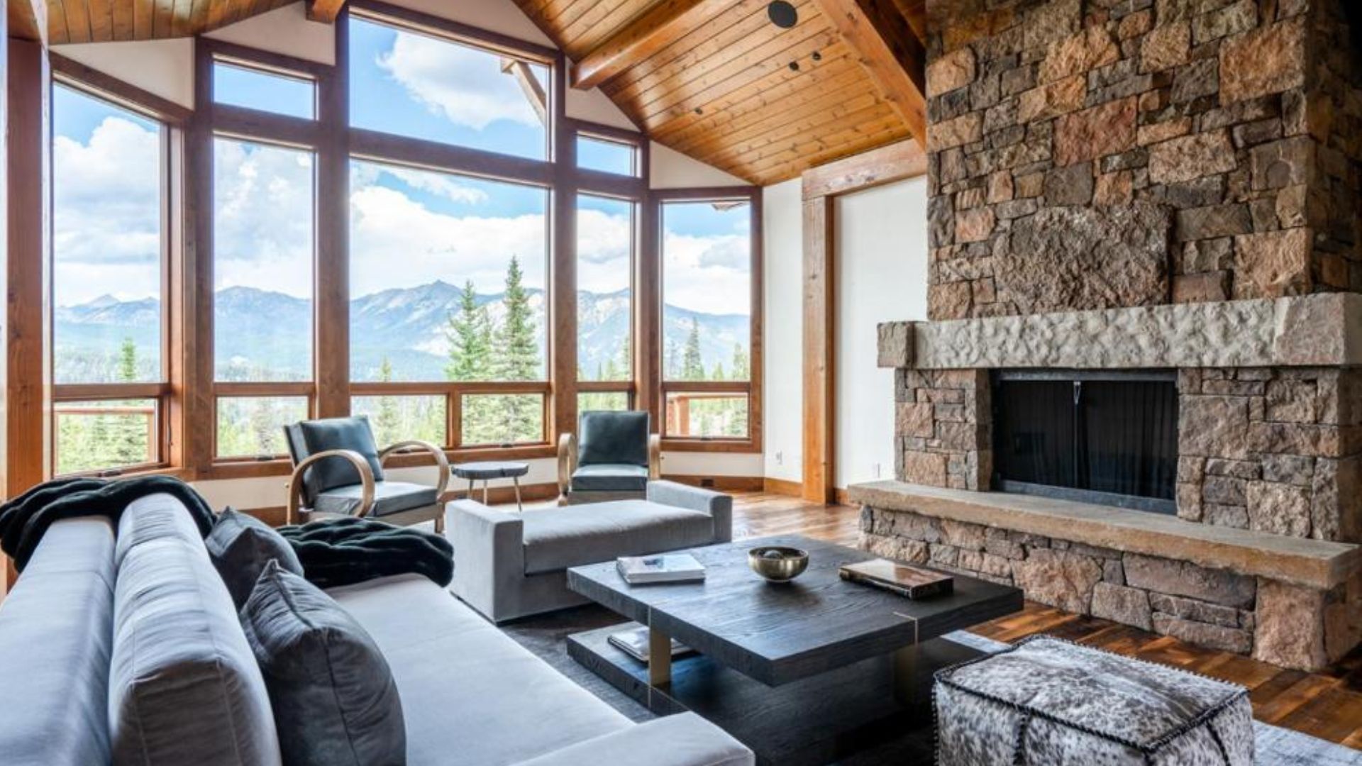 spacious living room with a modern grey sofa and table next to a huge fireplace and lots of natural light