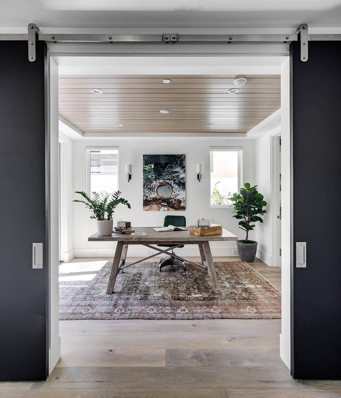 office area of a modern house with a brown desk, black chair, two windows and a patterned carpet