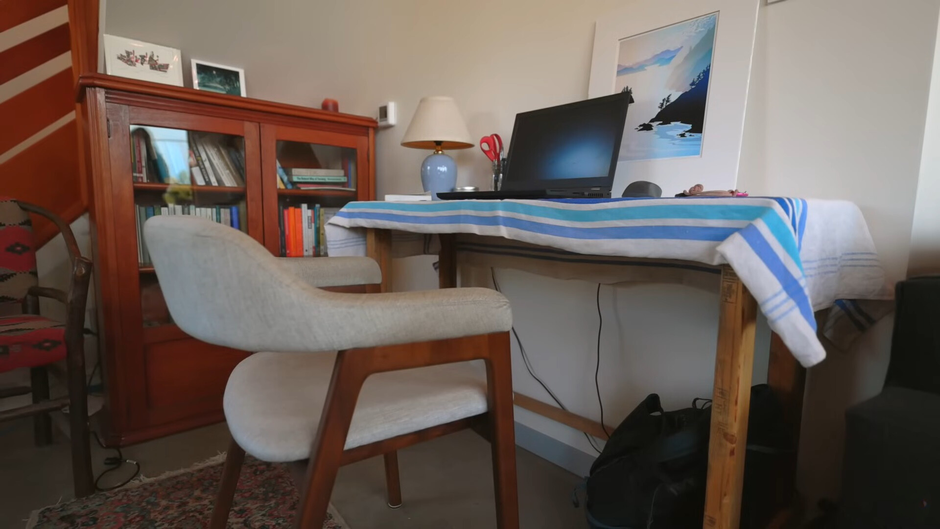 office area in a cabin under the staircase, a desk and a chair, brown cabinet with books next to the desk and a painting above it