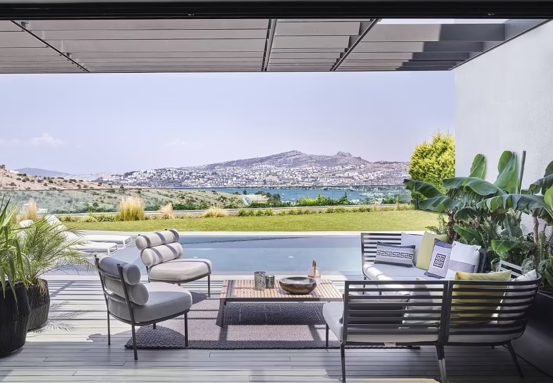 outside area of a modern house with cushioned seating, brown table and a pool with lawn around it