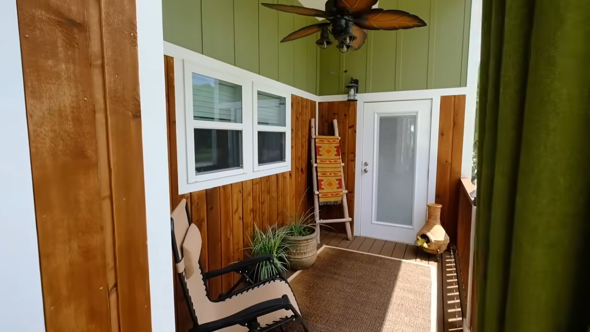 outdoors area of a tiny house with green and wooden walls and a fan on top