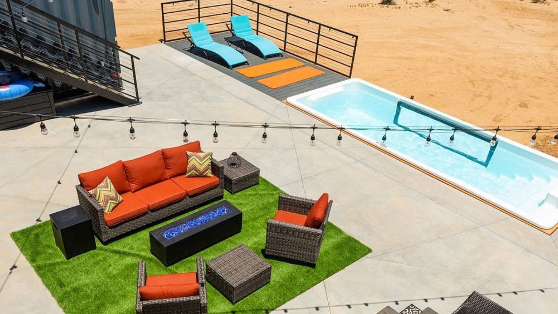 big patio with anthracite and orange patio furniture, light blue lounges, and a swimming pool