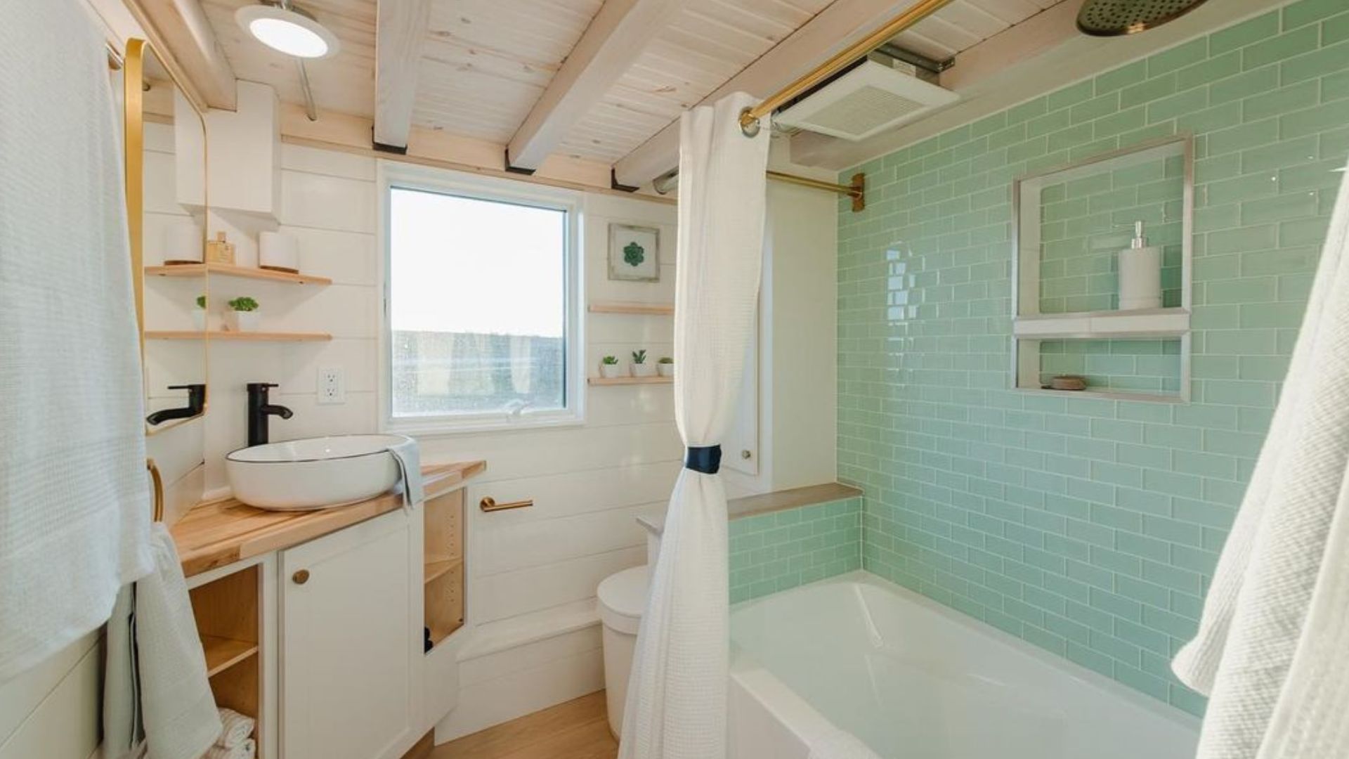 small bathroom in white with wood elements and beautiful green tiles in the bathtub