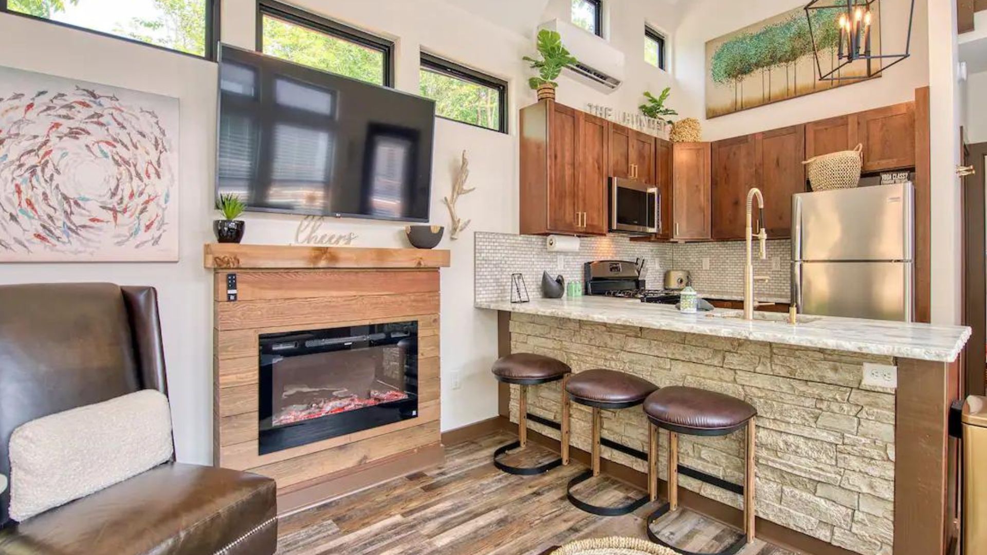 stone bar in kitchen with leather chairs, next to an electric fireplace with a decorative wooden planks around it