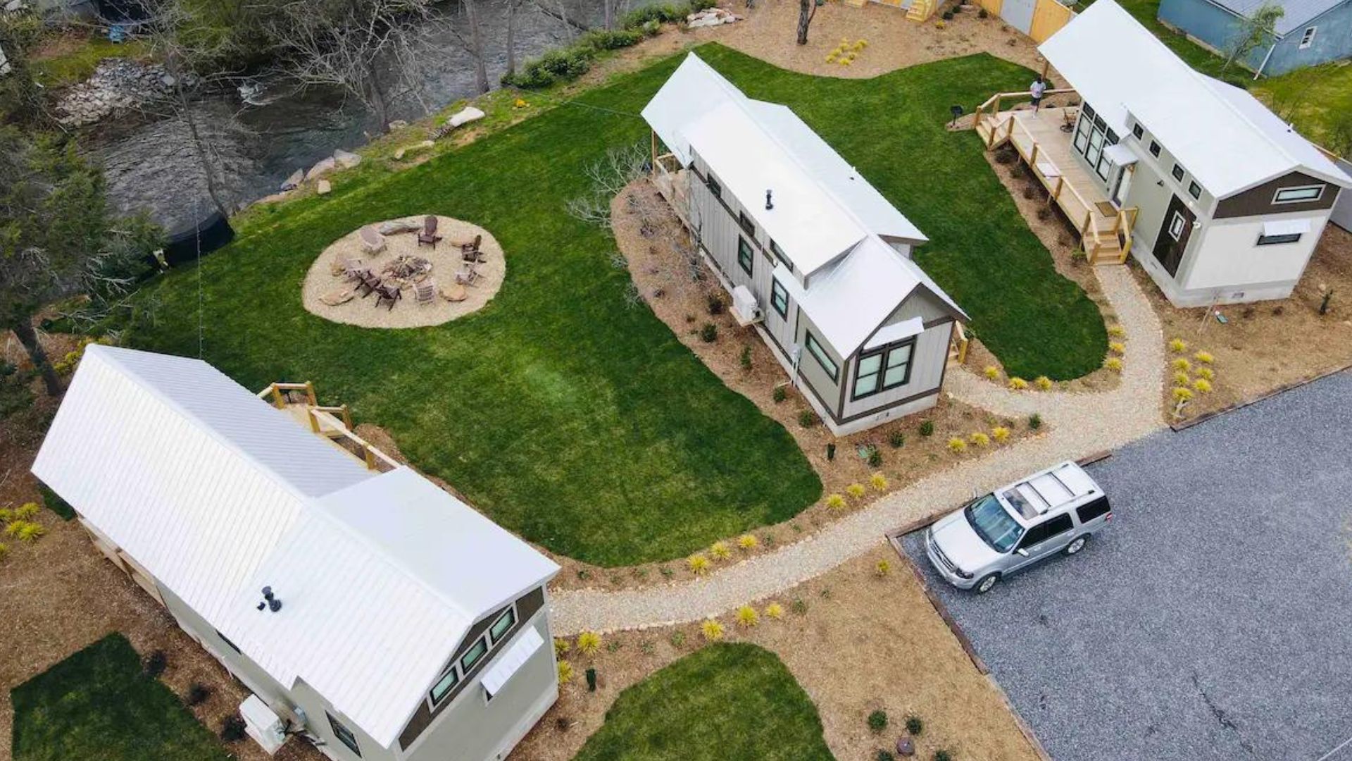 three tiny houses pictured from bird's point of view, nexxt to a river, and a car driveway