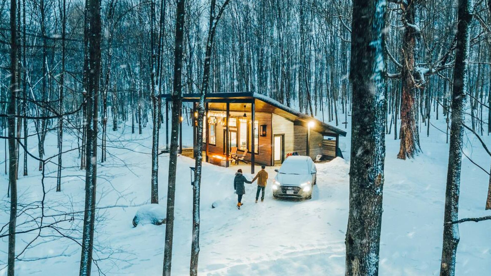 hickory outpost tiny house in snow with lights up and two people walking towards it