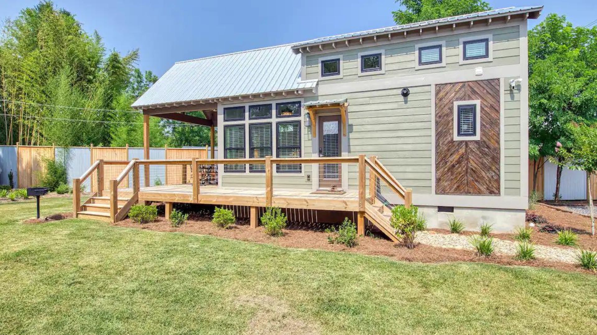 exterior of tiny house done in light mint green with green roof, lots of windows, and a small porch