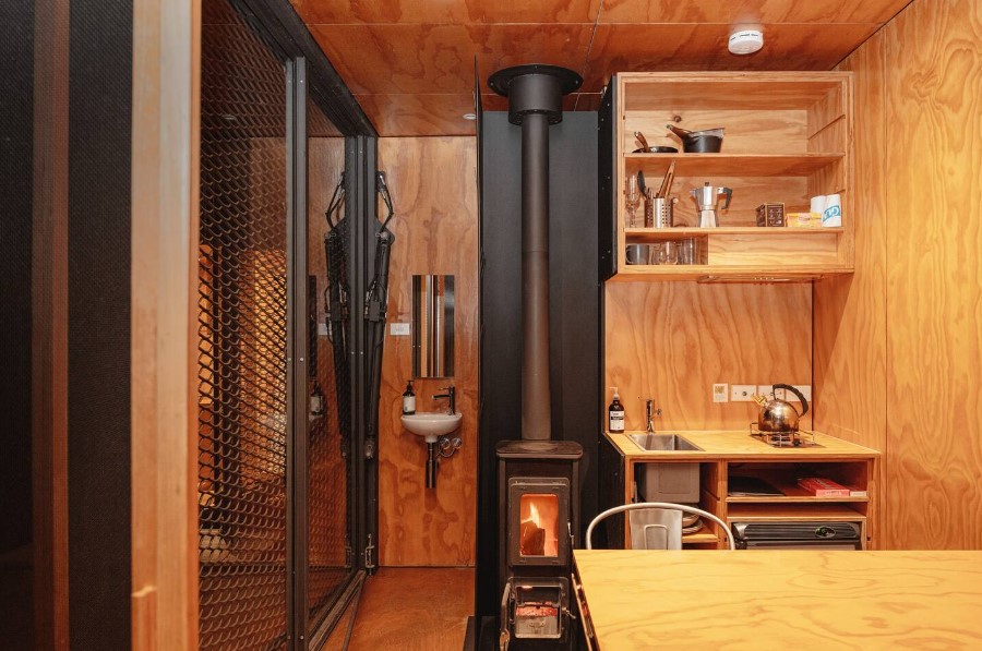 small kitchen of a container, shelves with amenities, small black fireplace, brown dining table