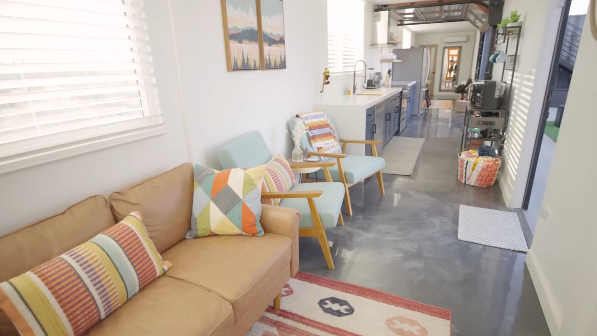 view from colorful living room with a brown couch and light blue armchairs and concrete floor