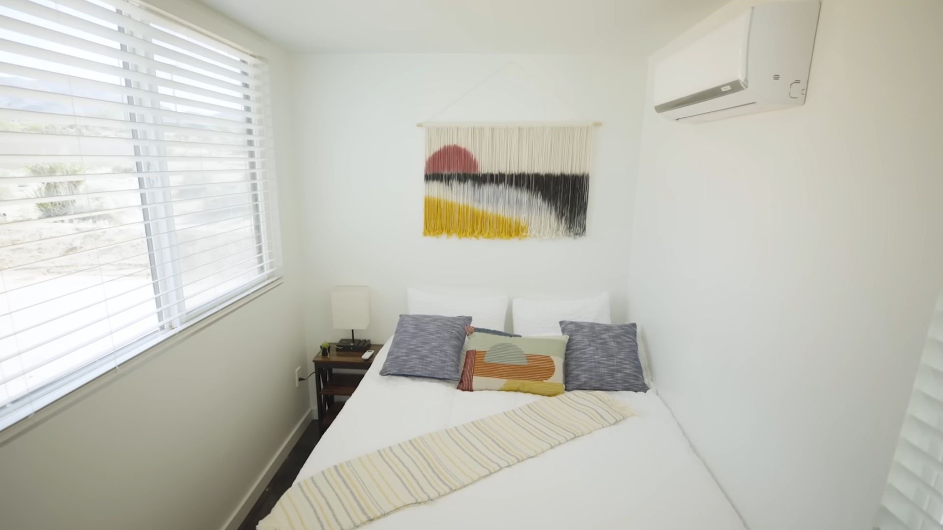 white guest bedroom with grey pillows and yellow details and some cool artwork on the wall