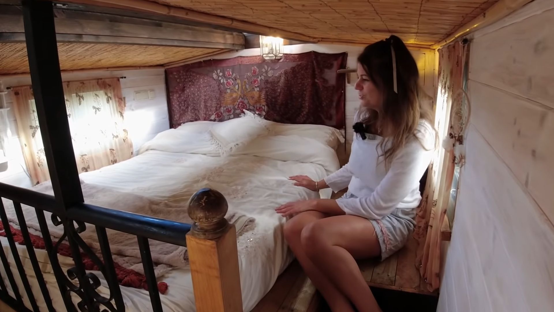 woman sitting on the floor next to her queen bed with a scarf headboard, lots of natural light coming from the roof windows