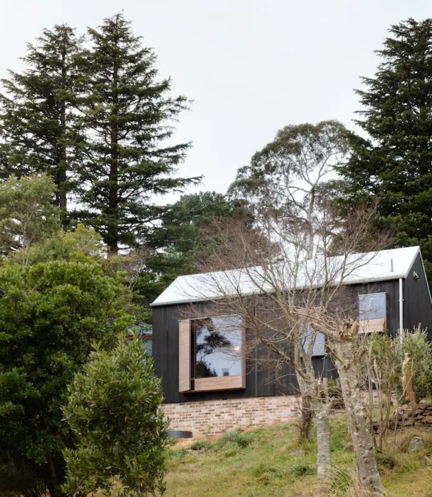 Black cabin in the woods with a white roof