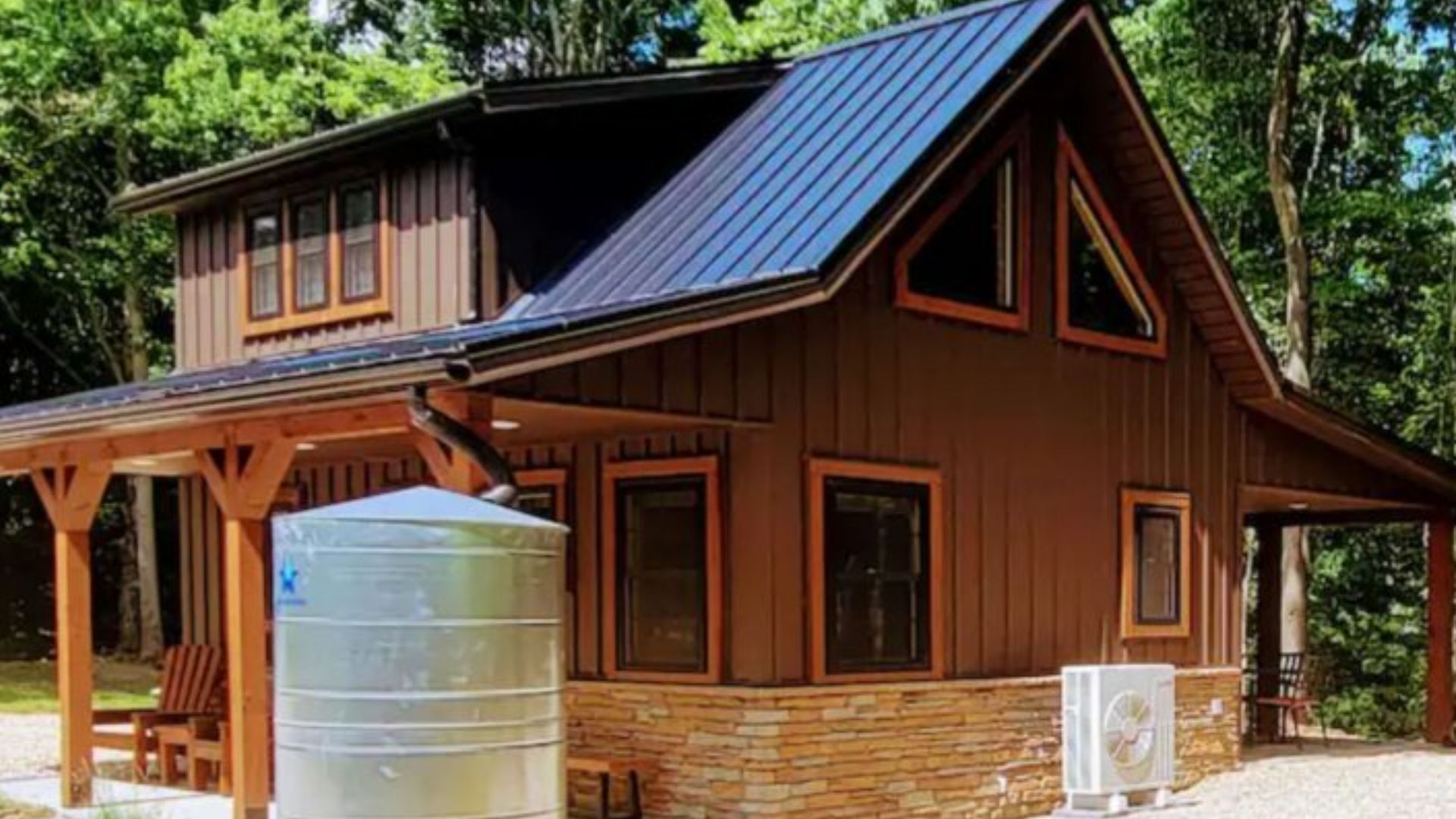 a small rustic cabin with a metal roof and a rainwater collection tank sits in a wooded area