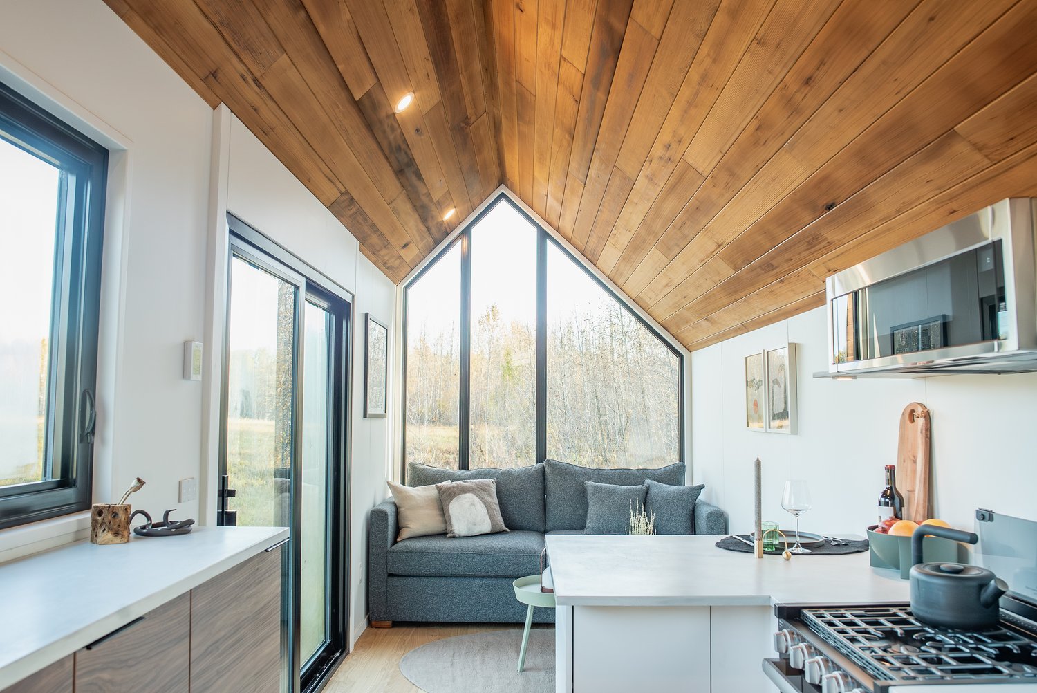 Living room of tiny house with huge widow, blue couch and wooden ceiling