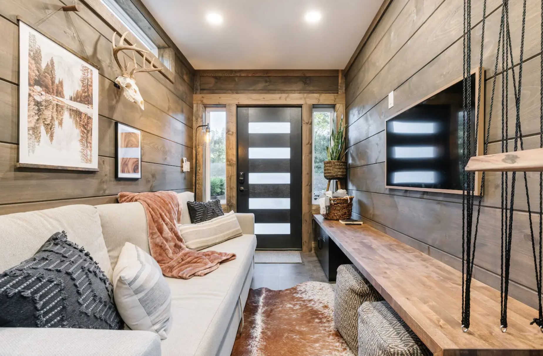 Living room with wooden boards, long white couch, wooden bench and a TV