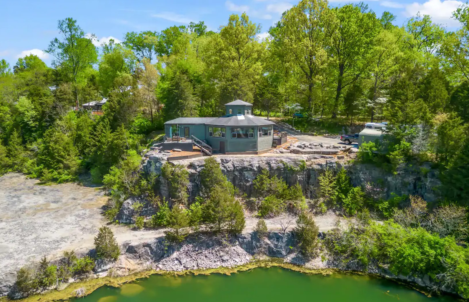 Green octagon cabin on a hill in front of a lake