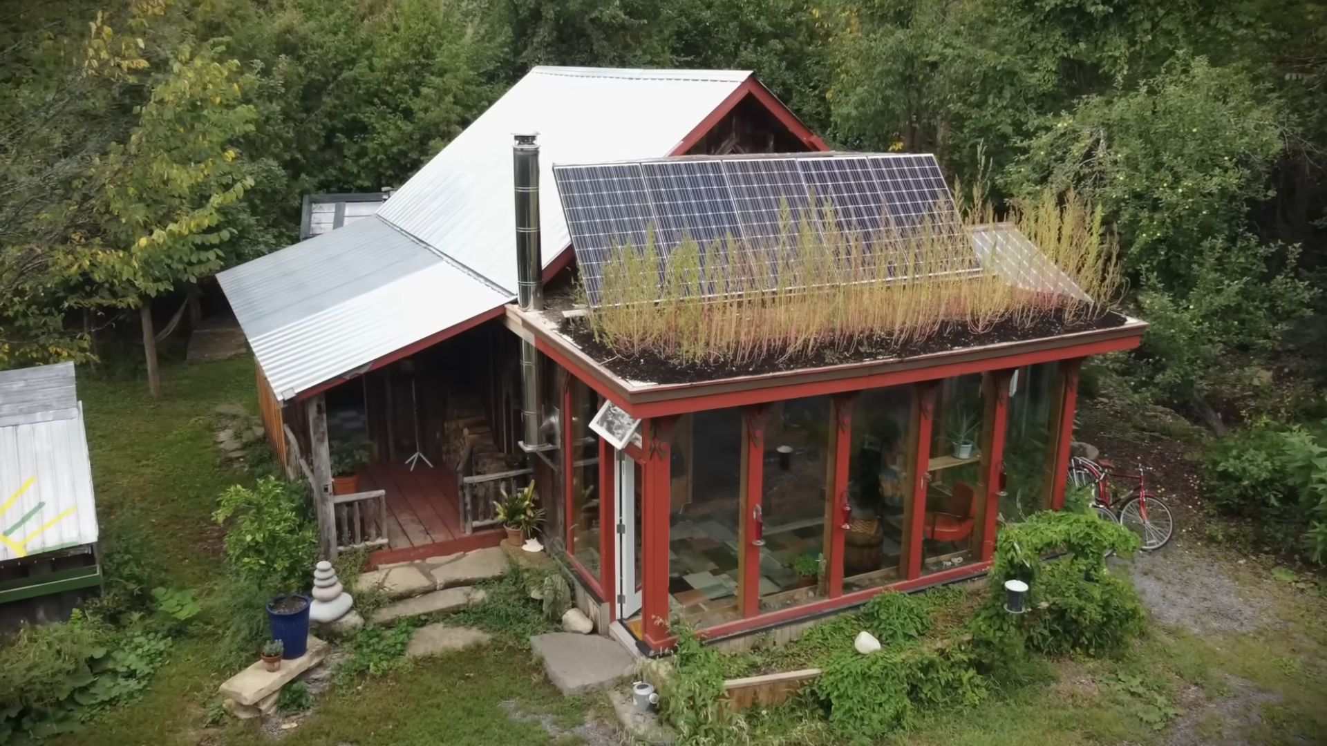 aerial view of the farm cabin in red, with solar panels, surrounded by forest and greenery