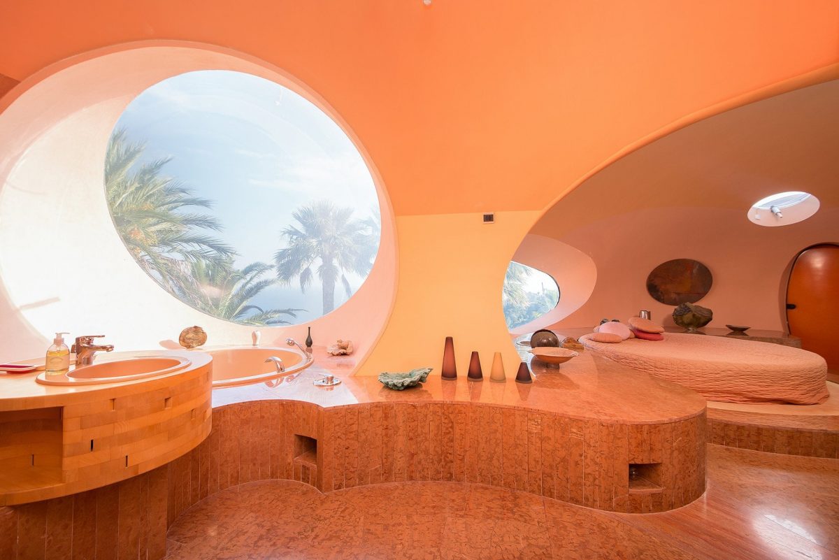 bathroom with a bathtub next to the round window and a bed in the background