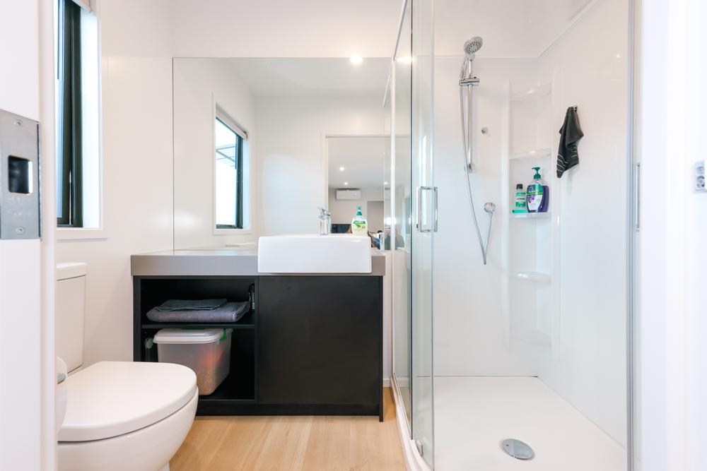 bathroom with a glass shower, white tiles, white toilet, black cabinet