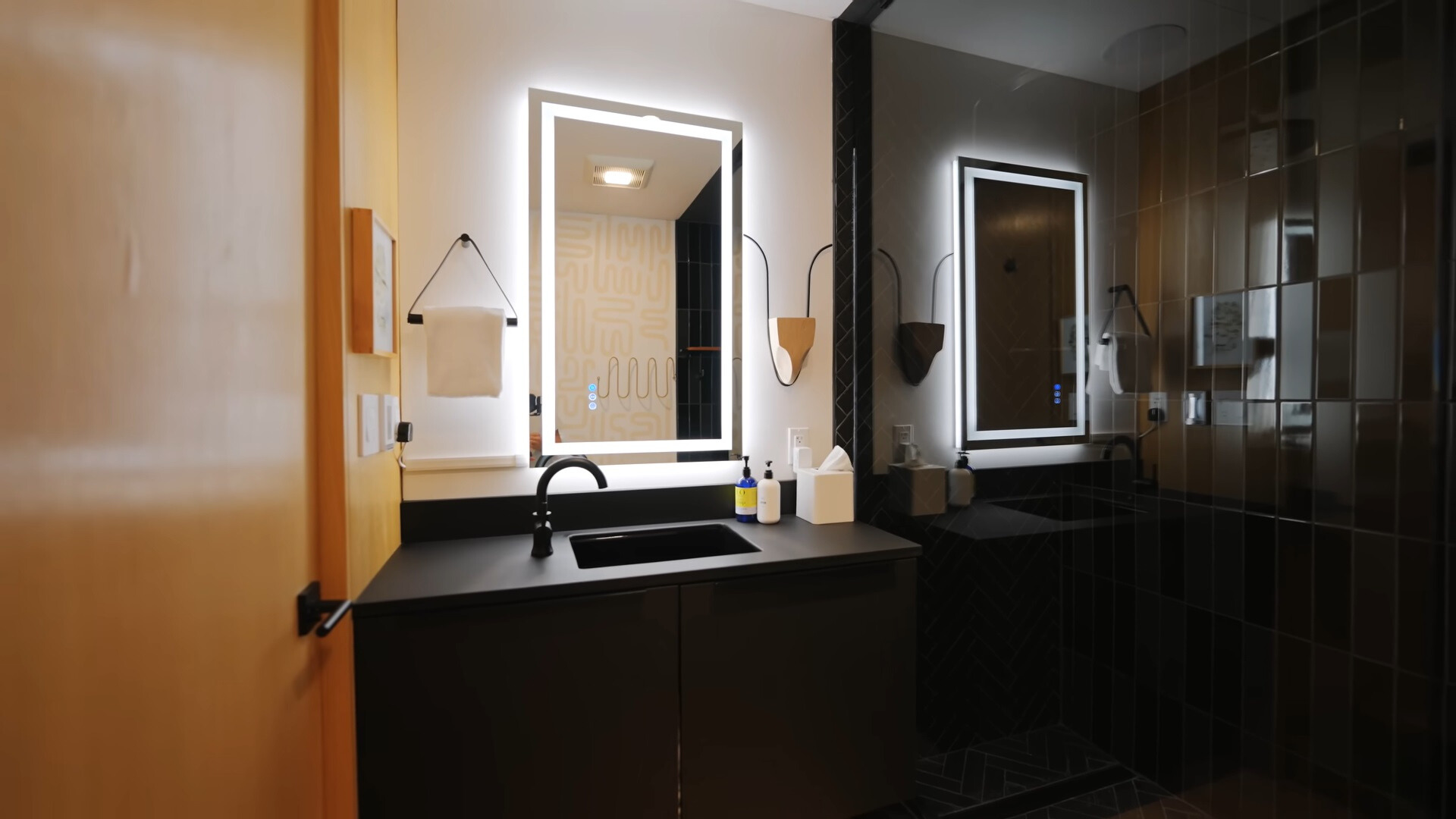 bathroom with black tiles, glass shower, and a mirror light and black cabinet