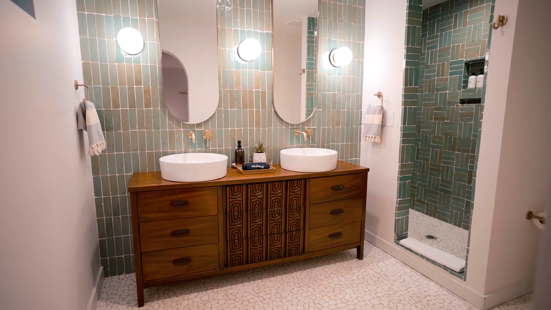 bathroom with green tiles, brown cabinet, oval mirrors and white sinks