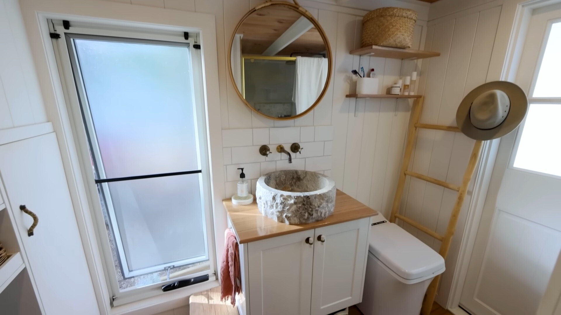 bathroom with a gray, textured sink, round mirror, white cabinet