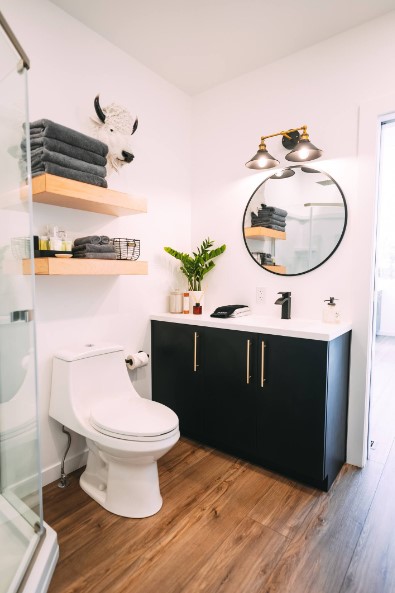 bathroom with a black cabinet, white countertop, round mirror above, light brown shelves and a cow head decor