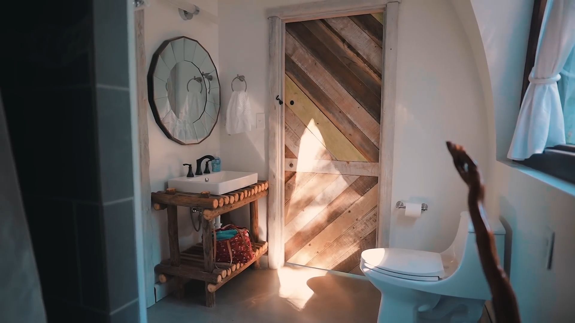 bathroom with a toilet and a unique vanity with a sink made of small wood logs, beautiful wooden door, a pretty mirror on the wall