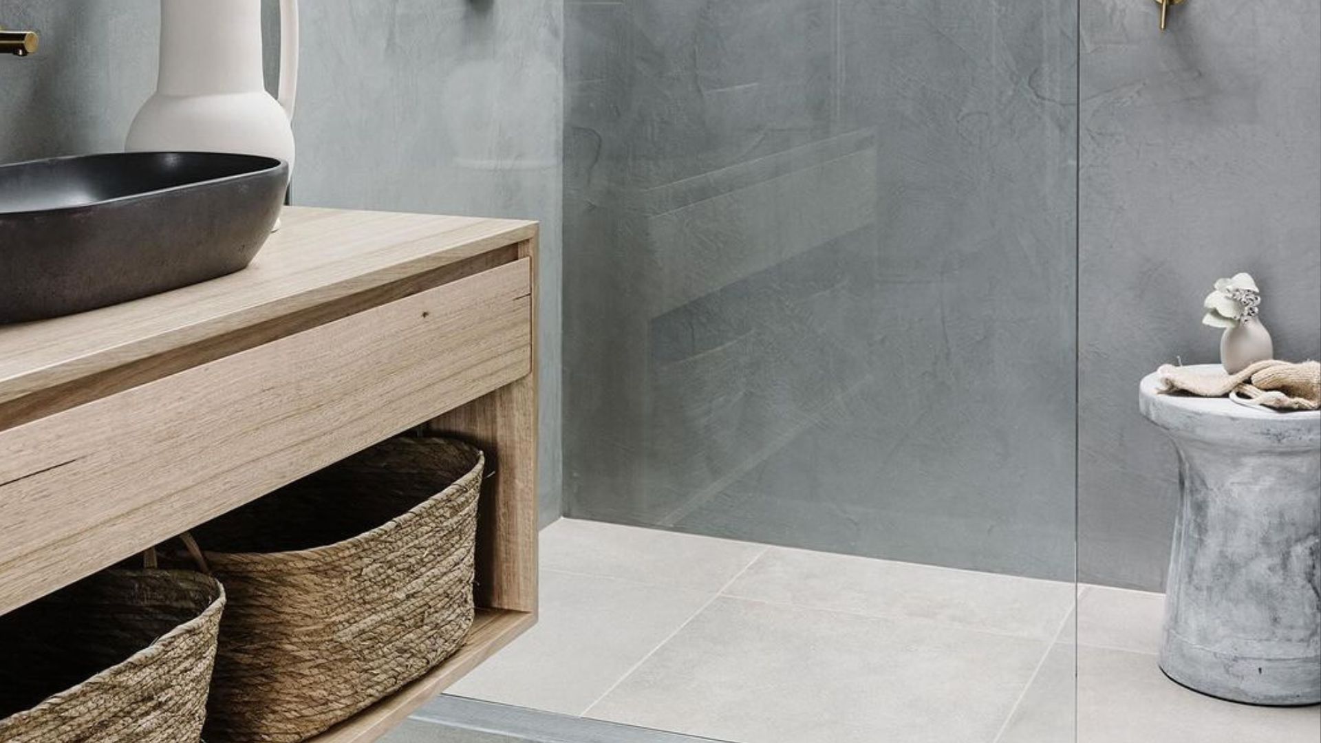 bathroom with concrede walls and floor, glass door, a wooden vanity with sink and baskets under it