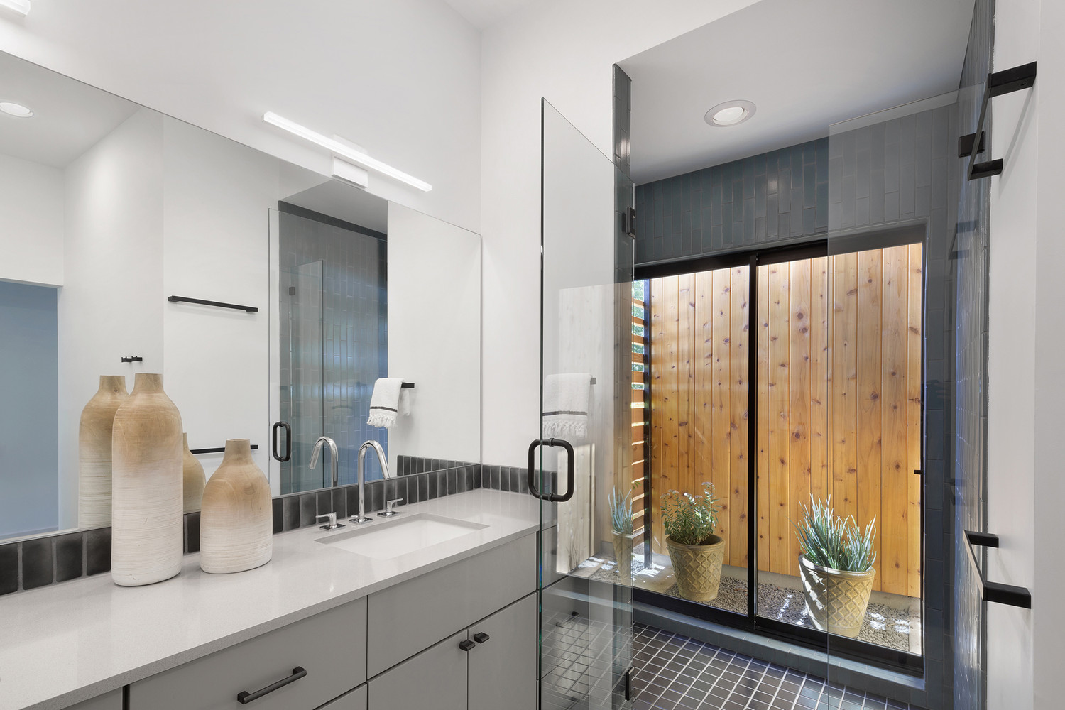 bathroom with a shower with gray tiles. light gray cabinets and a big mirror