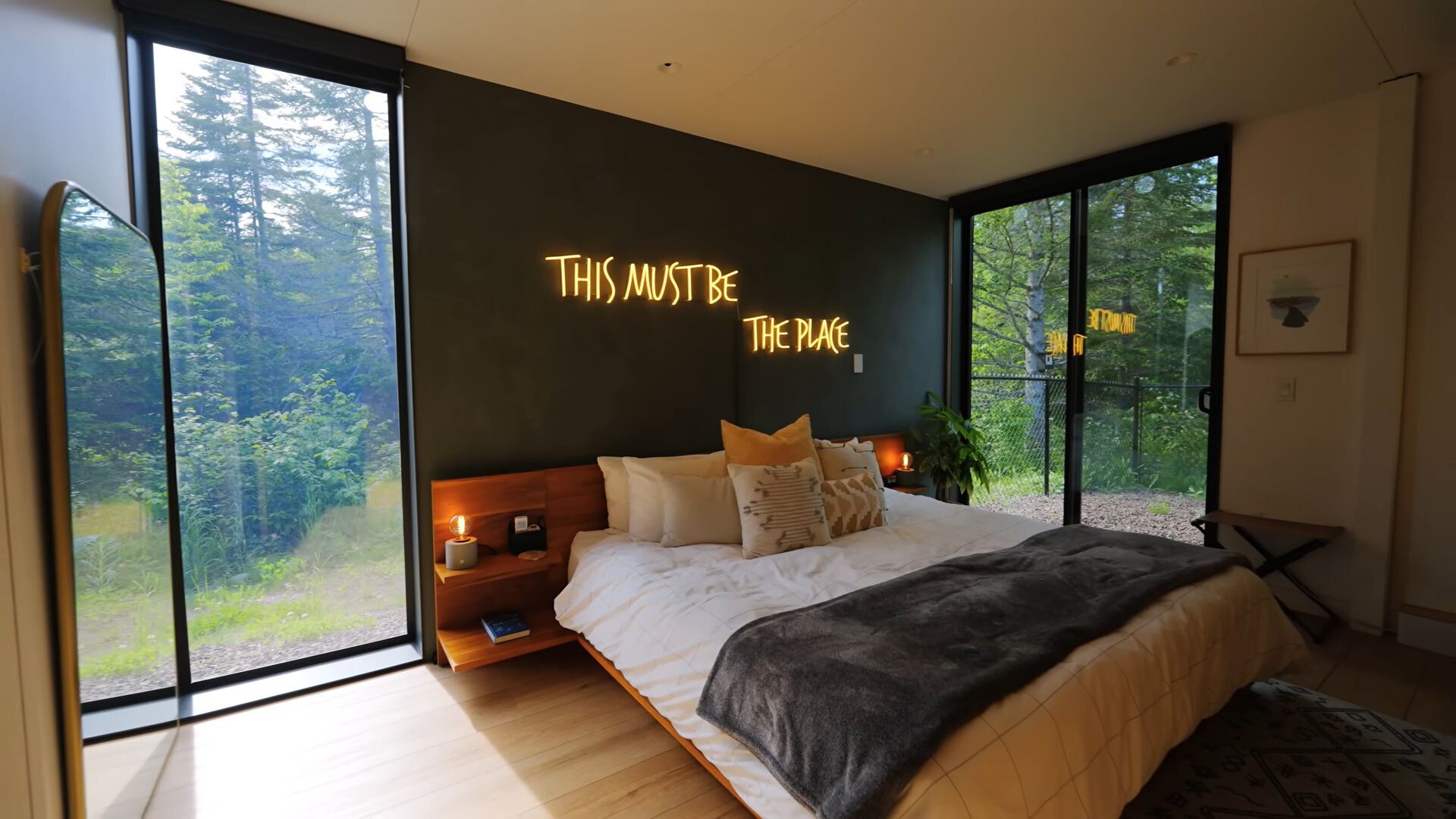 bedroom with a big bed and a neon sign above it, wooden bedside tables and floor to ceiling windows