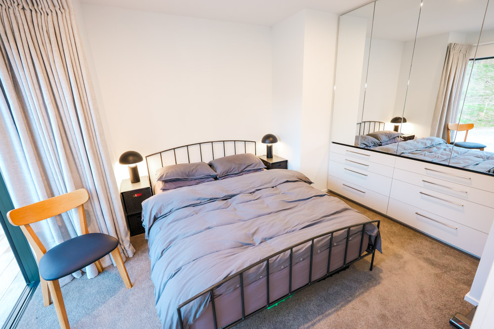 bedroom with a big bed, big closet with a big mirror and a floor to ceiling window and mushroom shaped lamps on bedside tables