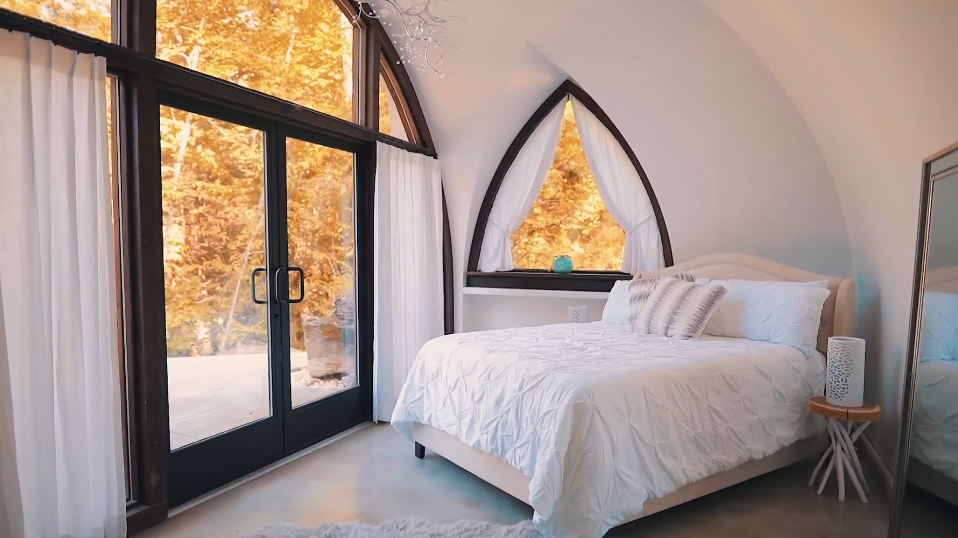 bedroom with a king bed and white bedding next to black frame windows and airy curtains