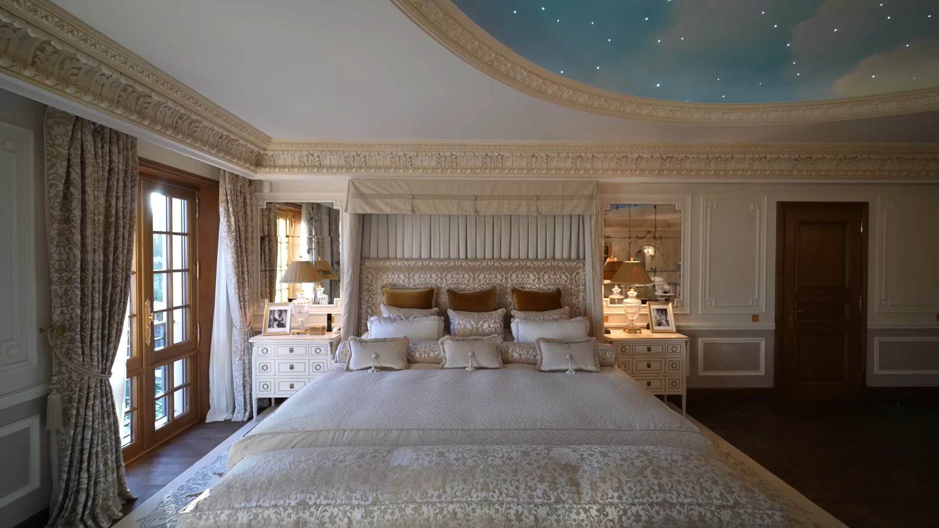 bedroom with a king sized bed with many pillows, white bedside tables and balcony doors next to the bed