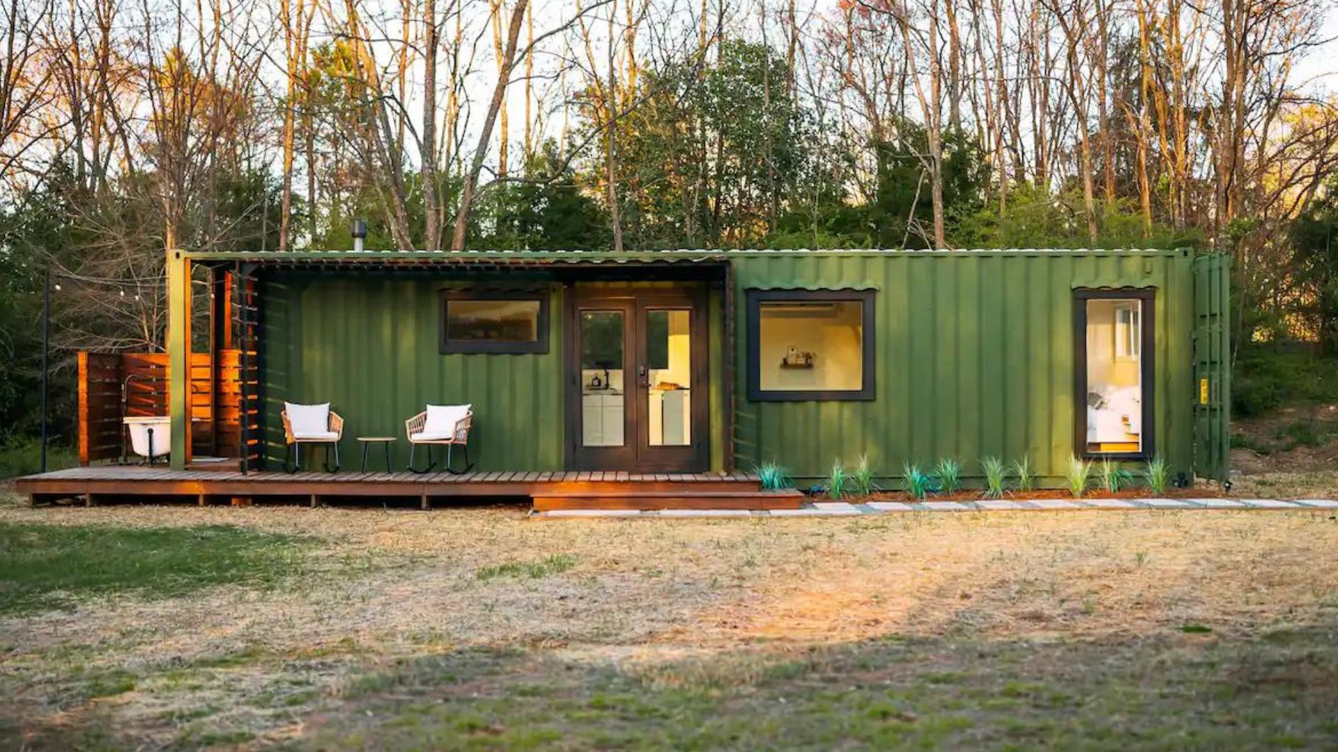 exterior of the forest green container with black frame windows and a covered porch, woods around it