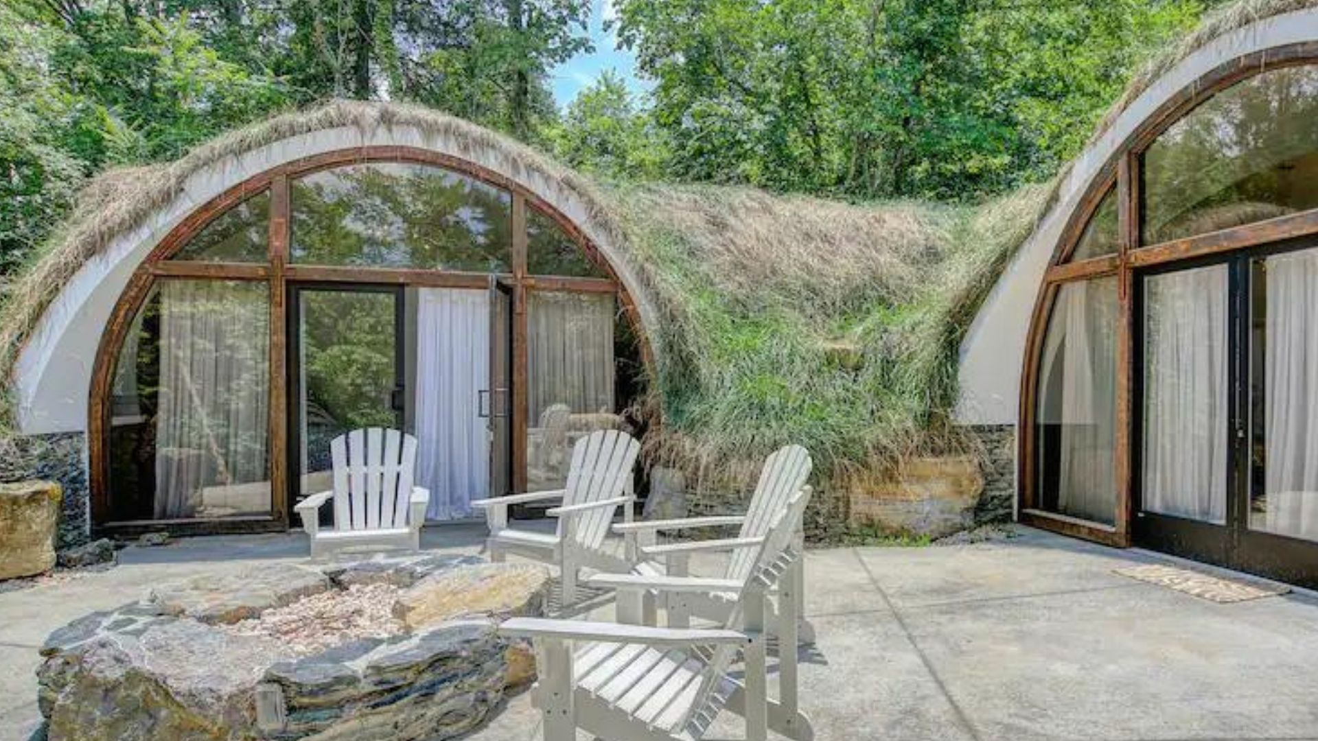 exterior of the modern hobbit-like house with semi round entrances, lots of black frame windows and doors, lounge chairs in front of the two entrances