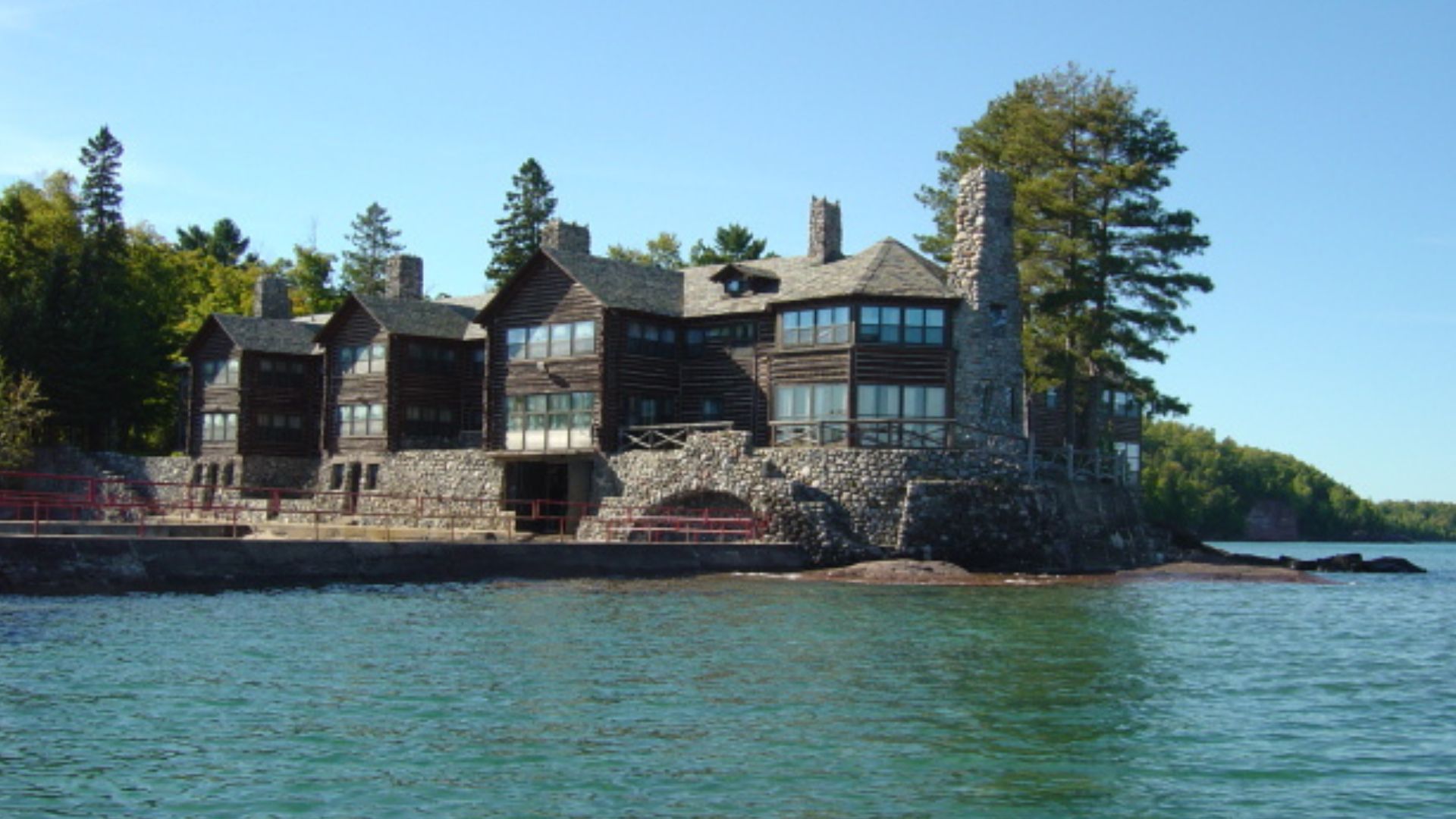 granot loma, a historic stone and log mansion situated on a scenic waterfront surrounded by trees