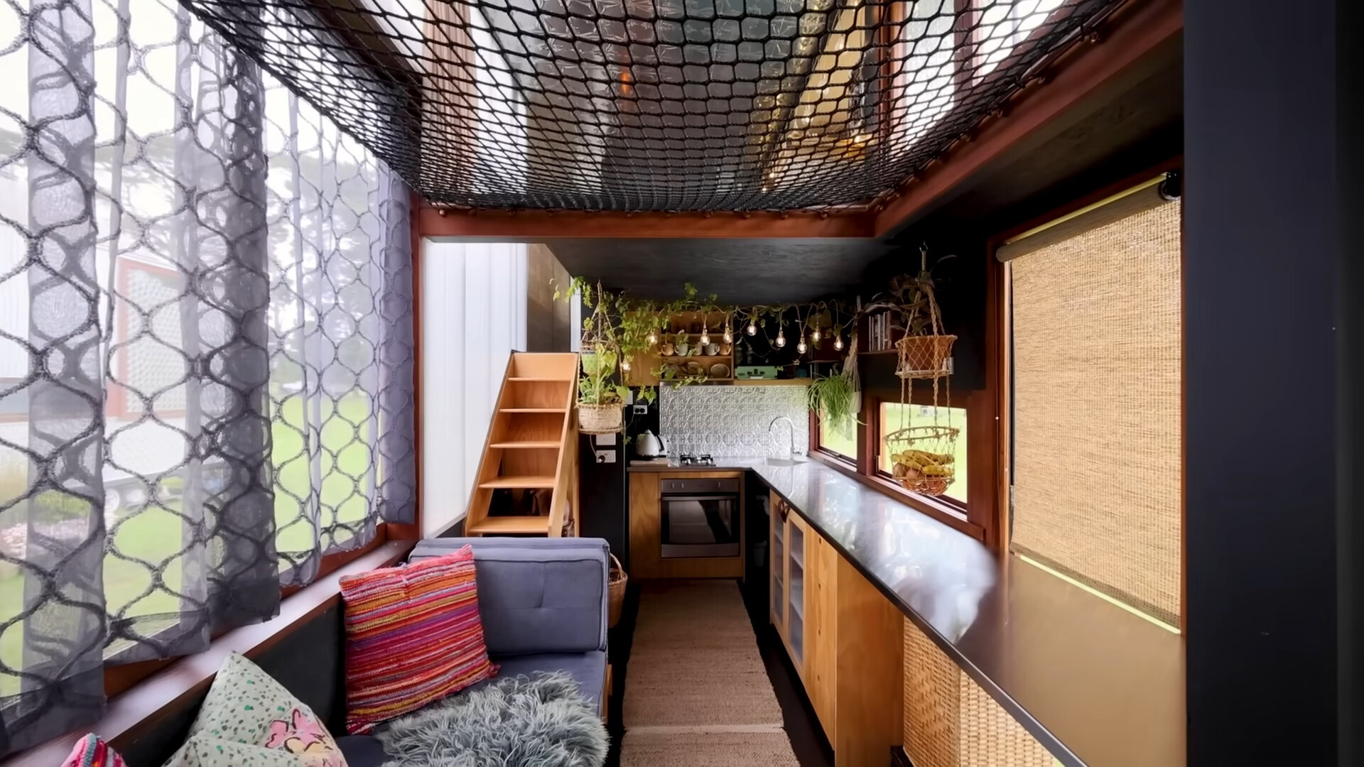 interior of a tiny house, blue couch with colorful pillows on the left and a long countertop on the right with plants at the back of the place