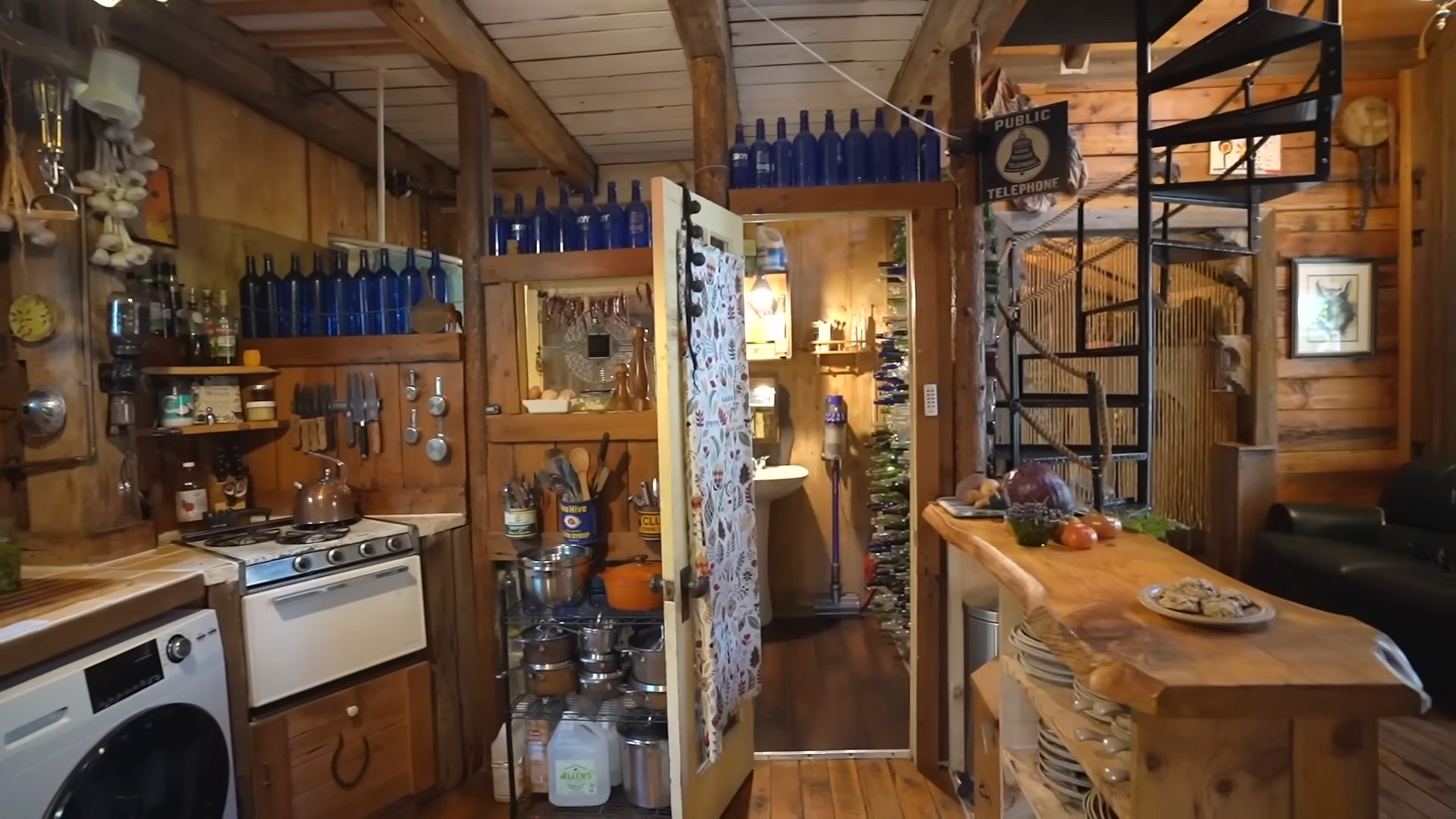 kitchen photographed from a different angle, visible waching machine and sink, spiral stairs on the right, a small wooden bar with shelves too